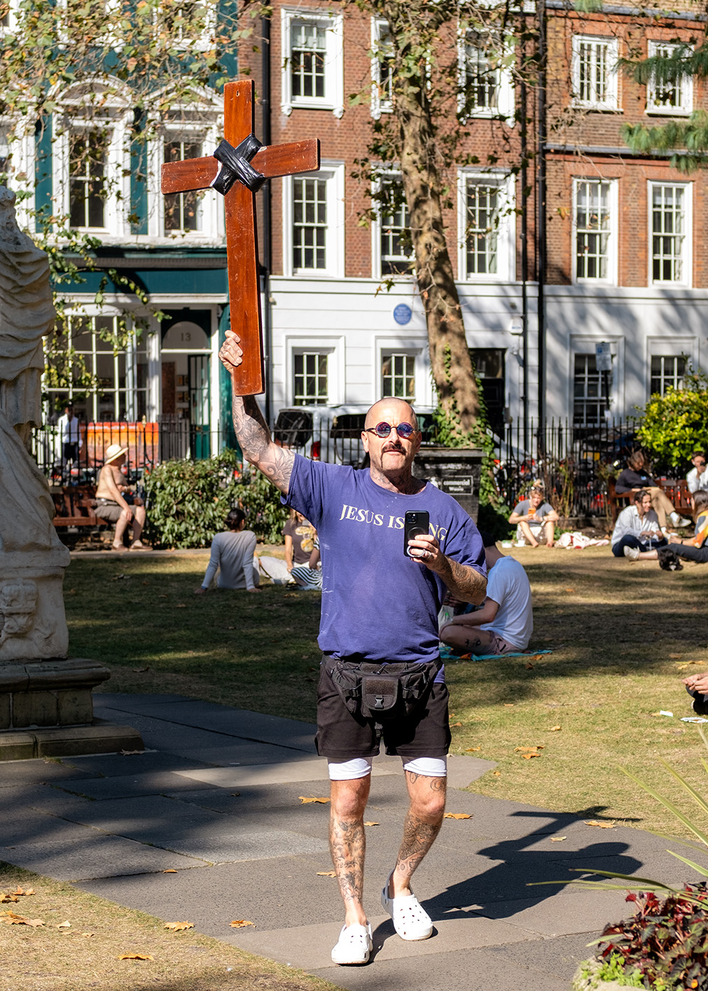 God preacher holds crucifix high up whilst walking through Soho Square, London