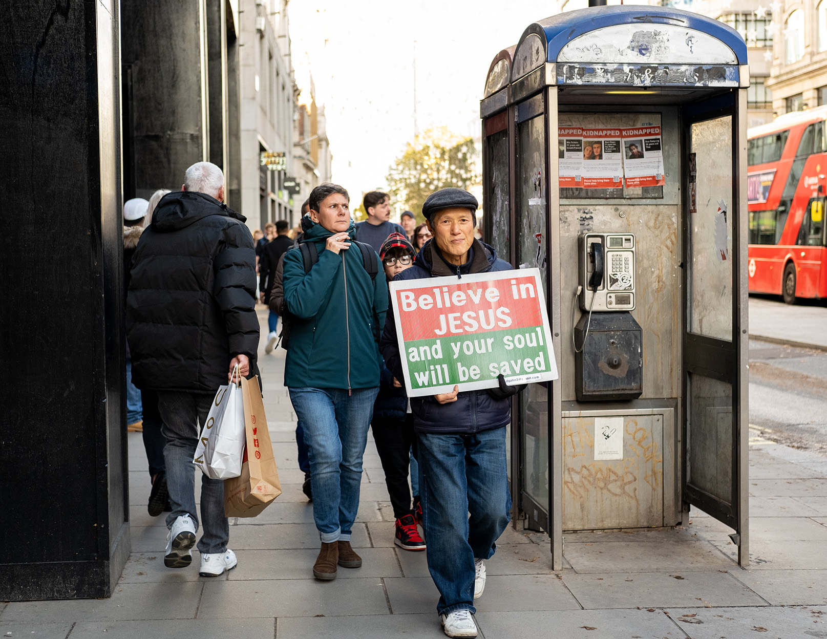 Chinese god preacher walks down oxford street holding 'believe in jesus' placard.