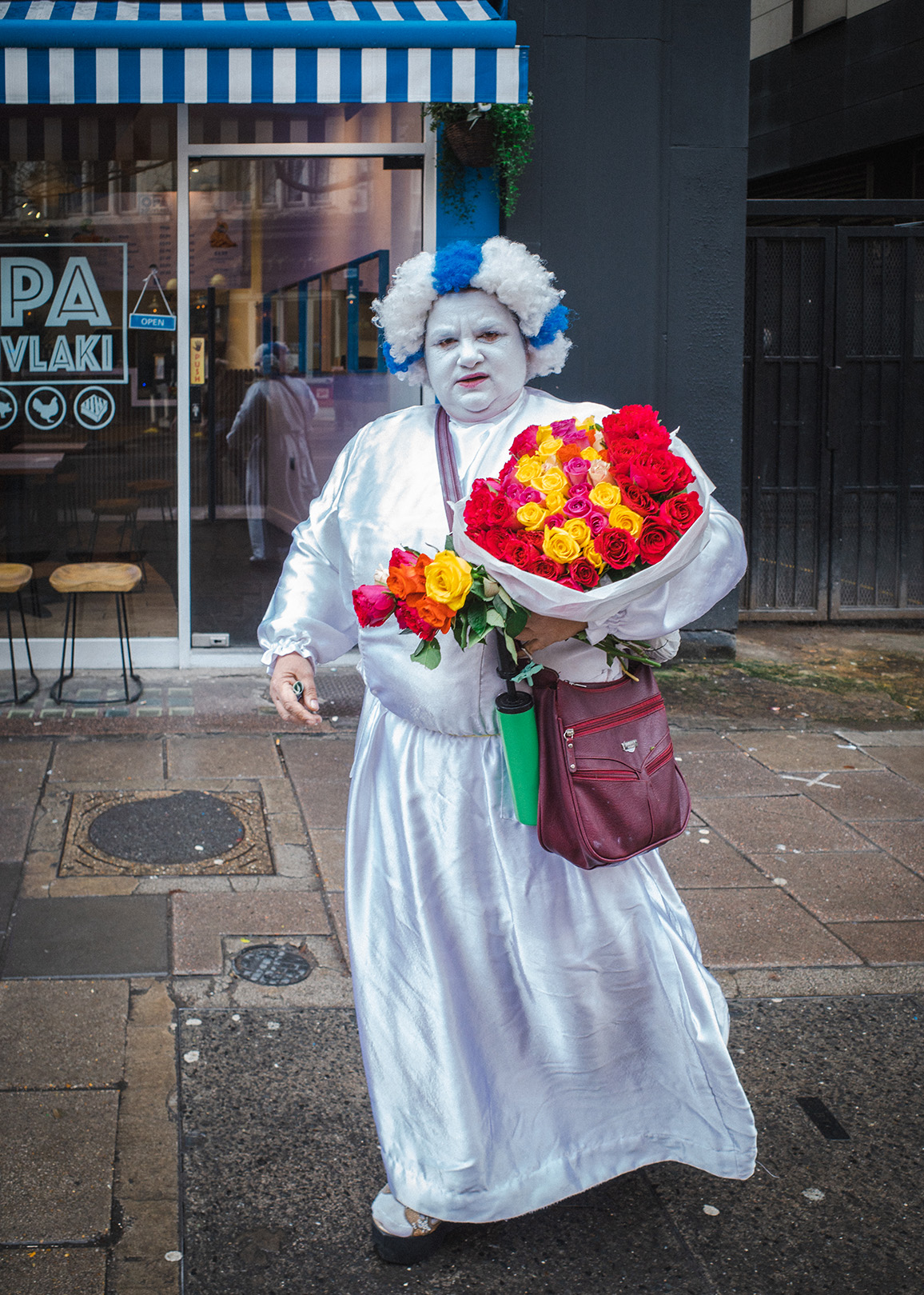 Man in strange fancy dress holds flowers.