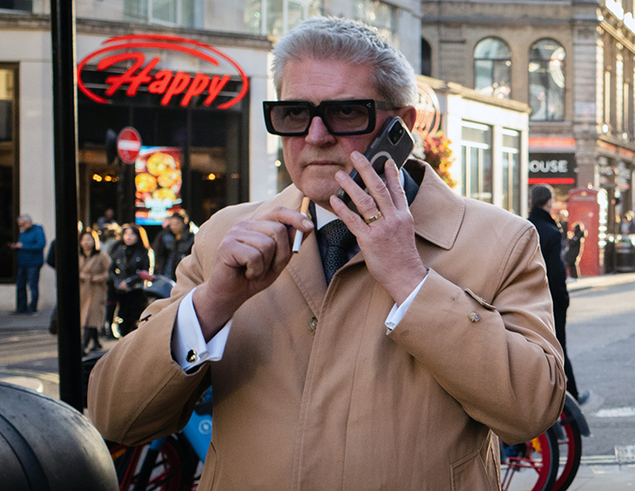 Man that looks like a gangster, holds a cigarette, Central London.