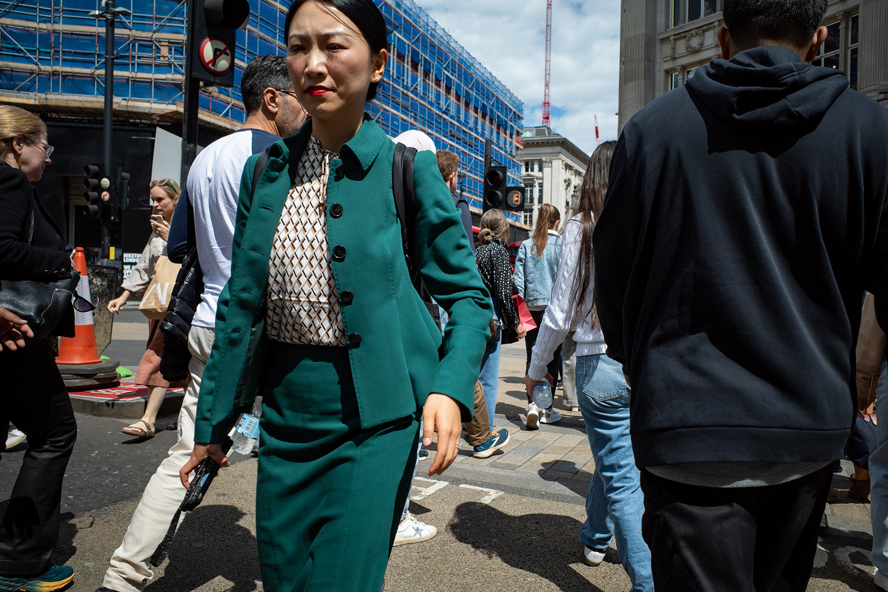 Woman in striking smart green suit walking across a busy oxford street, London.